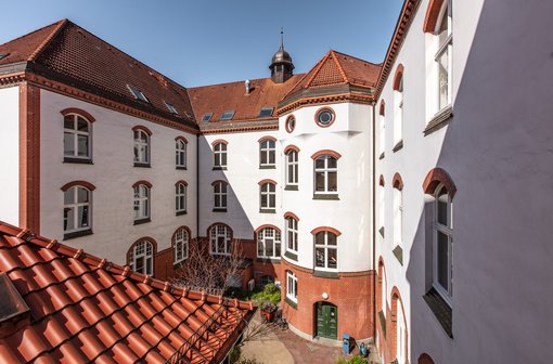 Innenhof des IFSH - Ein von weißen Gebäuden mit roten Ziegeldächern umgebener Hof mit mehreren Fenstern.